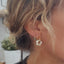 Boucles d’oreilles en acier inoxydable doré avec fleur effets nacre beige.